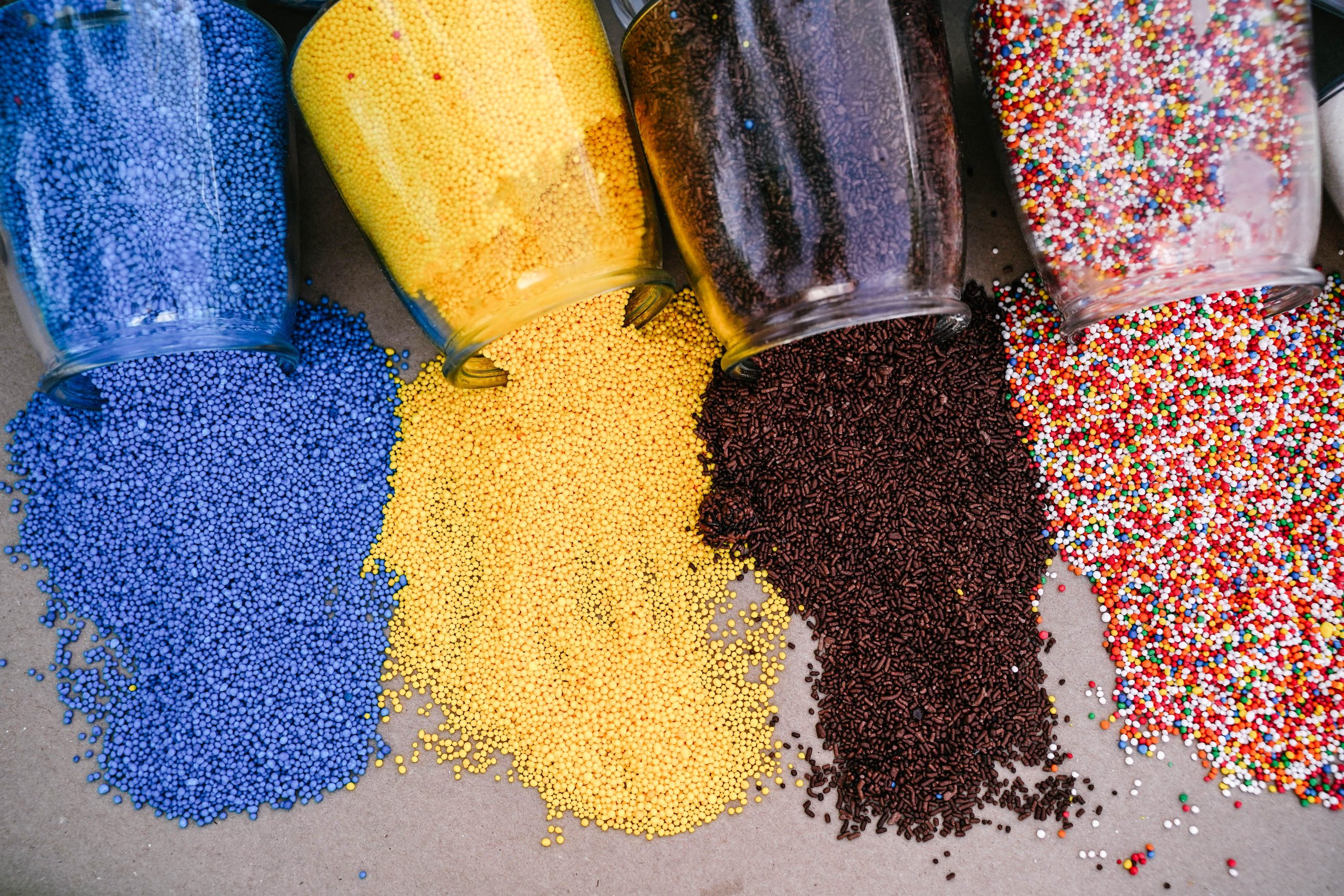 An overhead view of assorted colorful sprinkles and beads spilling from glass jars.